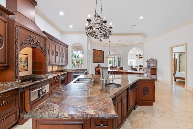 kitchen with pendant lighting, dark stone countertops, sink, and a large island with sink