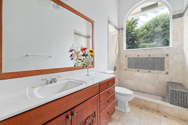 bathroom with toilet, a tile shower, vanity, and tile patterned floors