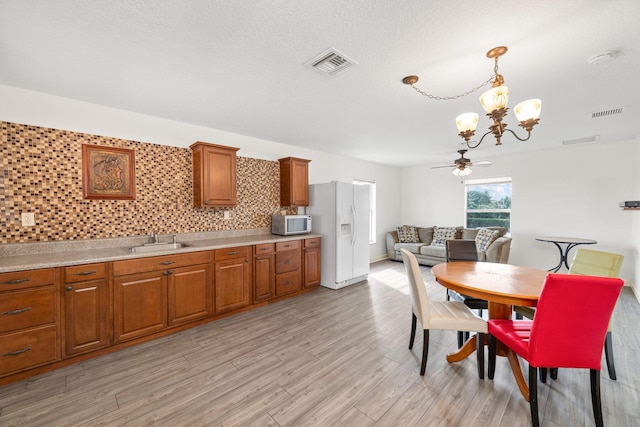 dining space featuring ceiling fan with notable chandelier, light hardwood / wood-style floors, and sink