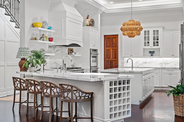 kitchen featuring decorative light fixtures, stainless steel double oven, a large island, light stone countertops, and white cabinets