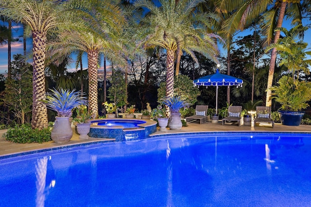 pool at dusk featuring an in ground hot tub and a patio area