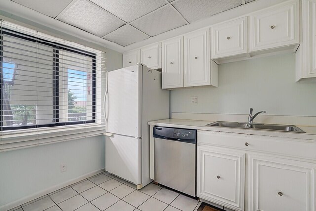 kitchen with appliances with stainless steel finishes, a paneled ceiling, sink, light tile patterned floors, and white cabinetry