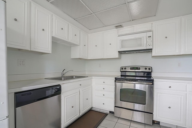 kitchen with a drop ceiling, sink, stainless steel appliances, light tile patterned floors, and white cabinets