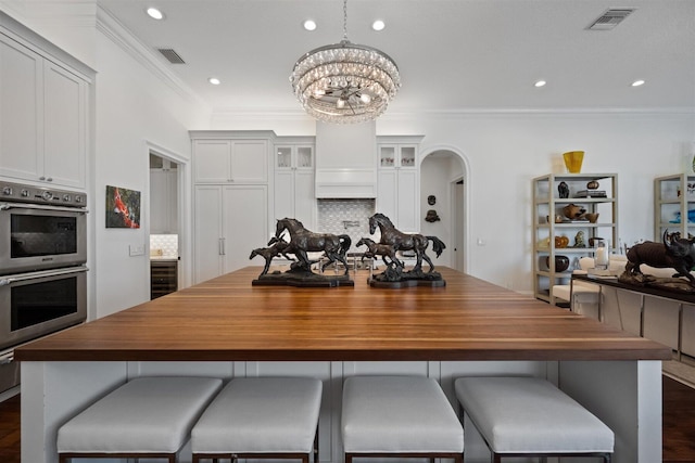 kitchen featuring an inviting chandelier, double oven, crown molding, decorative backsplash, and white cabinets