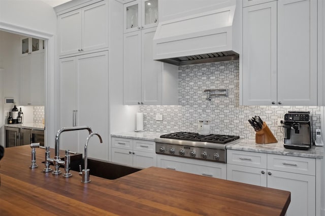 kitchen with custom exhaust hood, butcher block counters, backsplash, and stainless steel gas cooktop