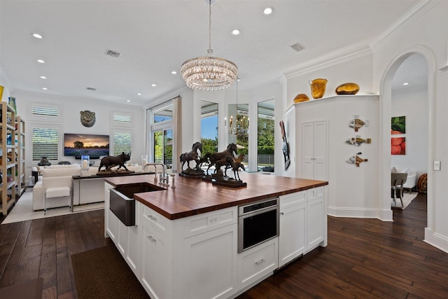 kitchen featuring pendant lighting, a kitchen island with sink, white cabinets, sink, and butcher block counters