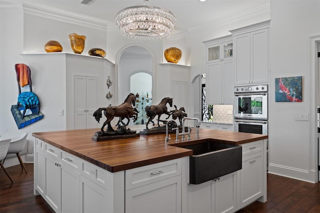 kitchen featuring white cabinets, sink, double oven, butcher block countertops, and a chandelier