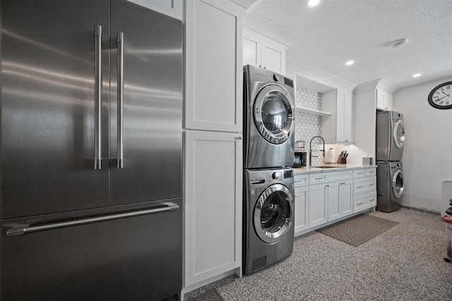 washroom with a textured ceiling, sink, and stacked washer and clothes dryer