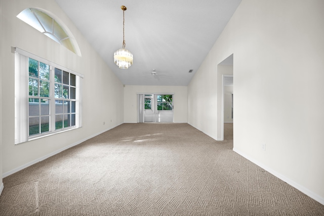 carpeted spare room featuring ceiling fan with notable chandelier and vaulted ceiling