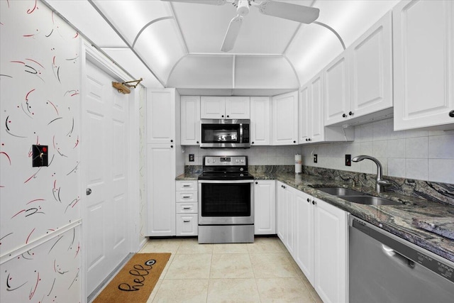 kitchen with dark stone counters, white cabinetry, a sink, light tile patterned floors, and stainless steel appliances