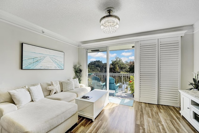 living area featuring a textured ceiling, light wood-type flooring, a chandelier, and crown molding