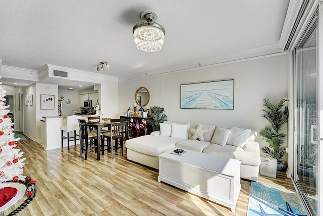 living room featuring light wood-style floors, visible vents, a chandelier, and ornamental molding