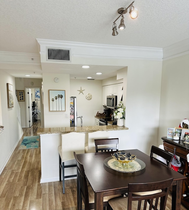 dining area featuring crown molding, light hardwood / wood-style floors, and a textured ceiling