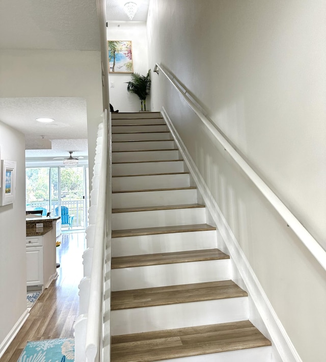 stairs with hardwood / wood-style flooring, ceiling fan, and a textured ceiling