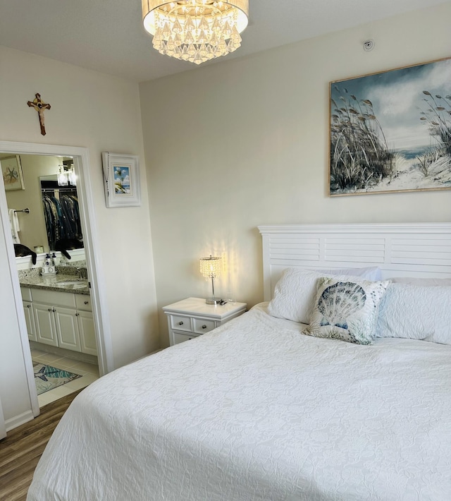 bedroom featuring an inviting chandelier, hardwood / wood-style floors, and ensuite bath