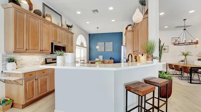 kitchen featuring kitchen peninsula, an inviting chandelier, decorative light fixtures, and light wood-type flooring