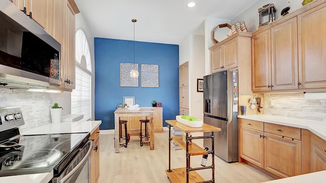 kitchen with appliances with stainless steel finishes, backsplash, light brown cabinetry, decorative light fixtures, and light hardwood / wood-style flooring