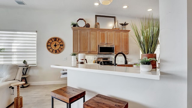 kitchen with kitchen peninsula, appliances with stainless steel finishes, light wood-type flooring, and tasteful backsplash