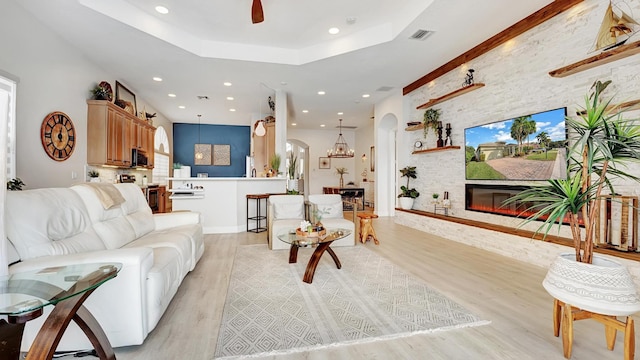 living room featuring a raised ceiling, light hardwood / wood-style flooring, ceiling fan, and a stone fireplace