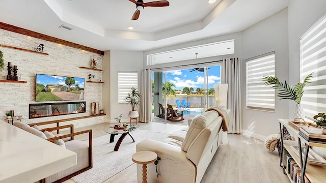 living room featuring a tray ceiling, ceiling fan, a fireplace, and light hardwood / wood-style floors