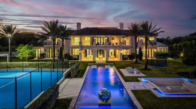 back house at dusk featuring a swimming pool with hot tub, a yard, a patio area, and a balcony