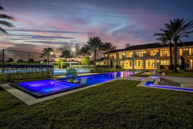 pool at dusk with an in ground hot tub and a lawn