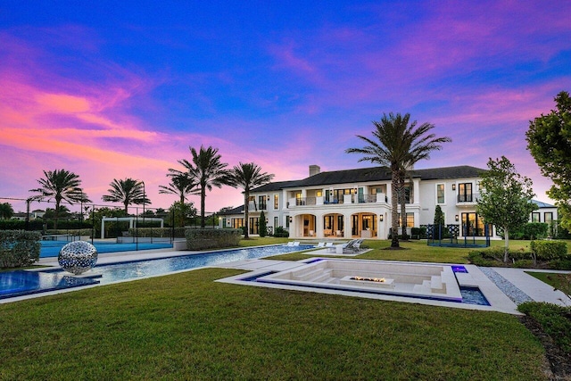 pool at dusk with tennis court and a lawn