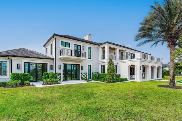 rear view of property with a yard, french doors, and a balcony