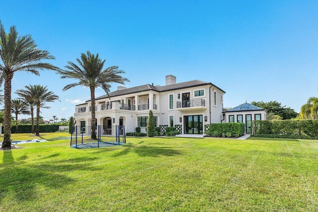 back of property with a balcony, a trampoline, and a lawn