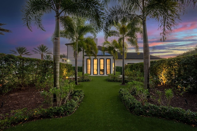 back house at dusk featuring a lawn