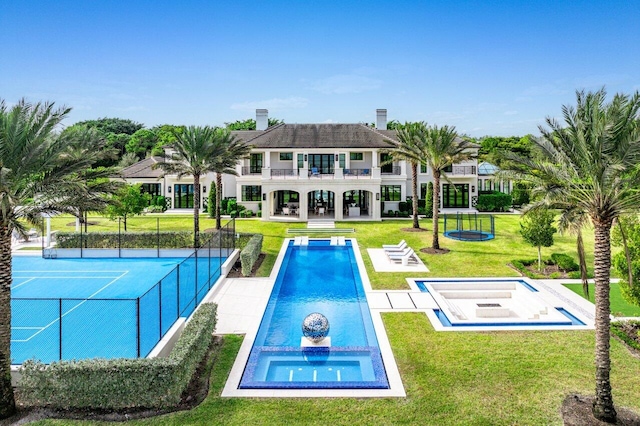 rear view of property with a balcony, tennis court, and a lawn