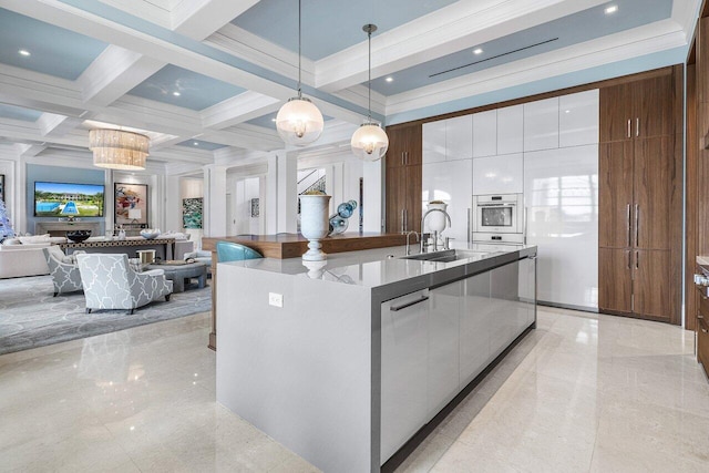 kitchen with sink, decorative light fixtures, a center island with sink, beamed ceiling, and white cabinets