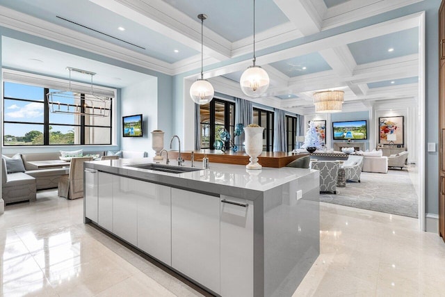 kitchen with pendant lighting, sink, white cabinets, a kitchen island with sink, and beam ceiling