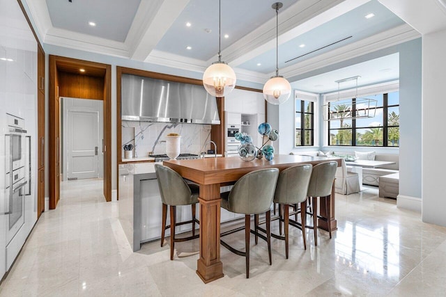 kitchen featuring pendant lighting, backsplash, range hood, ornamental molding, and white cabinets