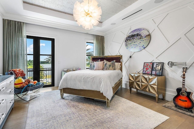 bedroom featuring hardwood / wood-style flooring, a notable chandelier, access to exterior, a raised ceiling, and french doors