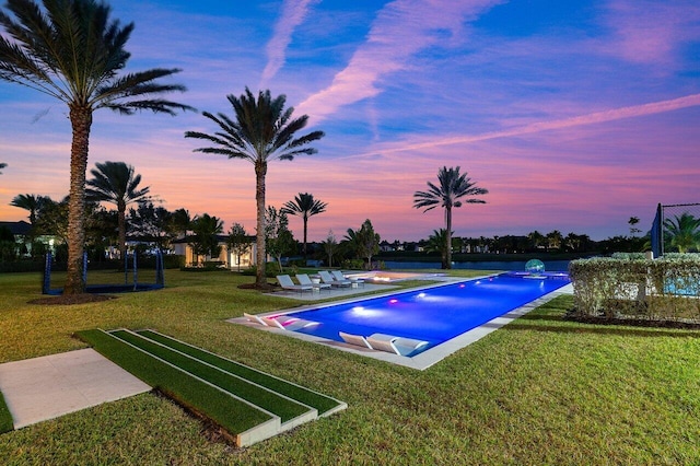 pool at dusk featuring a lawn