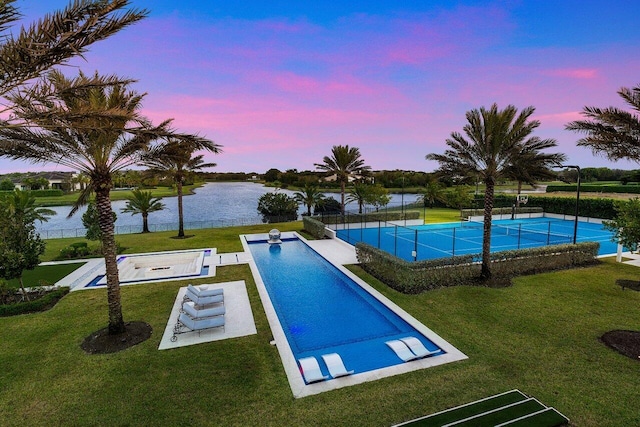 pool at dusk featuring a yard, tennis court, and a water view