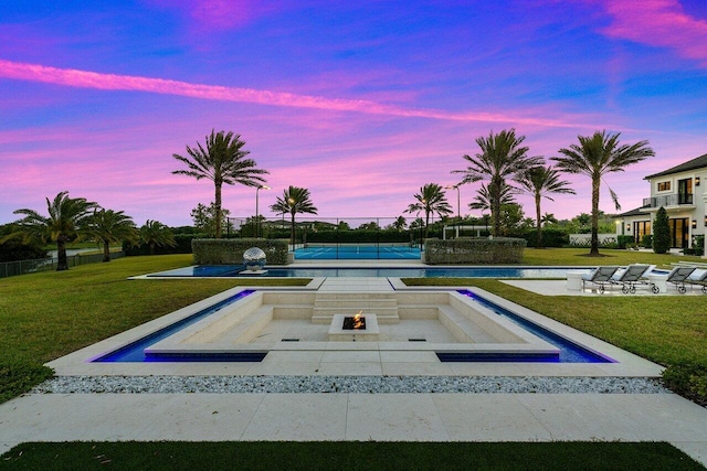 pool at dusk featuring a lawn and tennis court