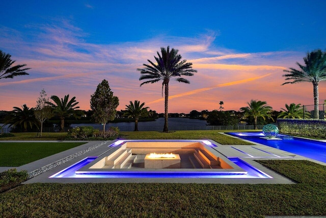 pool at dusk with an in ground hot tub and a yard