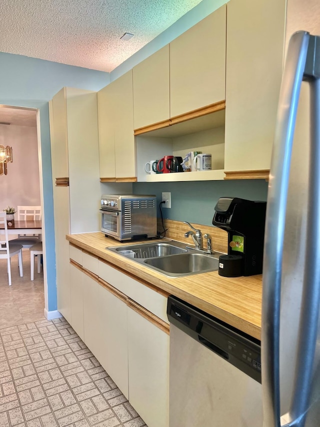 kitchen with sink, stainless steel appliances, a textured ceiling, and cream cabinetry