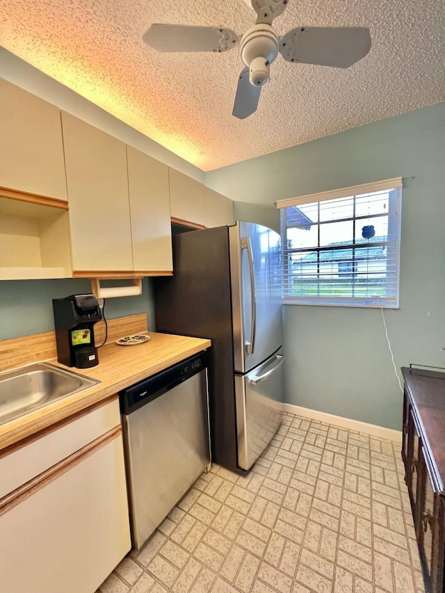 kitchen with wood counters, sink, ceiling fan, a textured ceiling, and stainless steel appliances