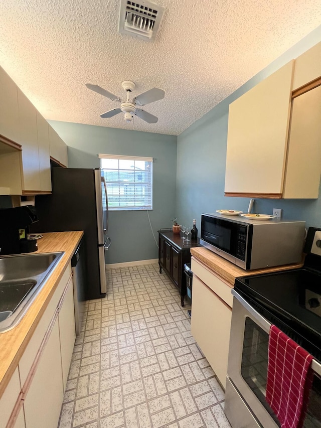 kitchen with appliances with stainless steel finishes, a textured ceiling, ceiling fan, sink, and butcher block countertops