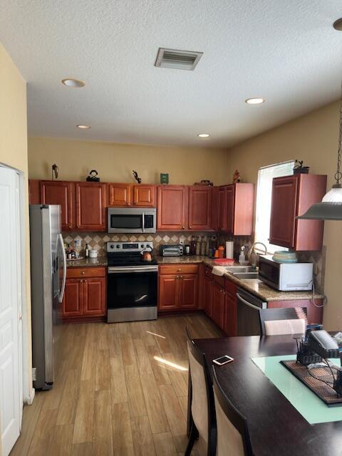 kitchen featuring pendant lighting, backsplash, sink, light hardwood / wood-style flooring, and stainless steel appliances