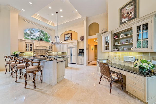 kitchen with hanging light fixtures, a high ceiling, cream cabinets, dark stone counters, and a kitchen bar