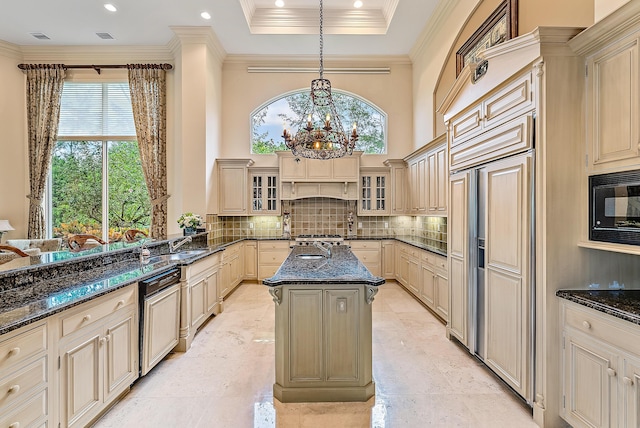 kitchen with hanging light fixtures, built in appliances, dark stone countertops, an island with sink, and tasteful backsplash