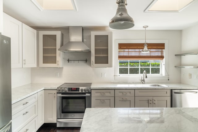 kitchen with light stone counters, sink, wall chimney exhaust hood, and stainless steel appliances