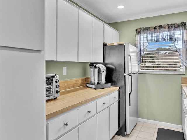 kitchen with light tile patterned floors, white cabinetry, ornamental molding, and stainless steel refrigerator