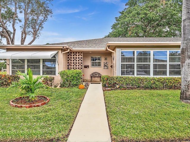 ranch-style home with stucco siding, a front yard, and roof with shingles