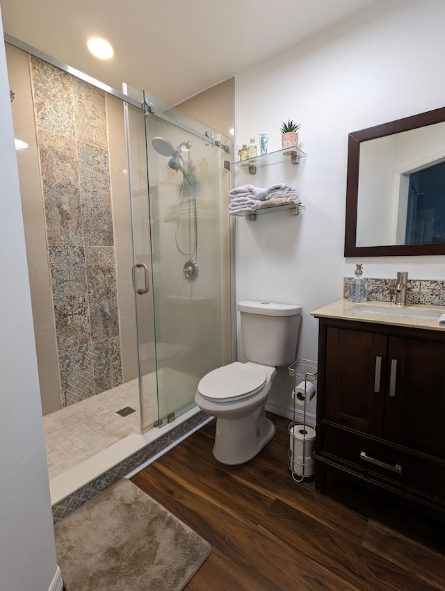 bathroom with toilet, vanity, a shower with shower door, and hardwood / wood-style flooring