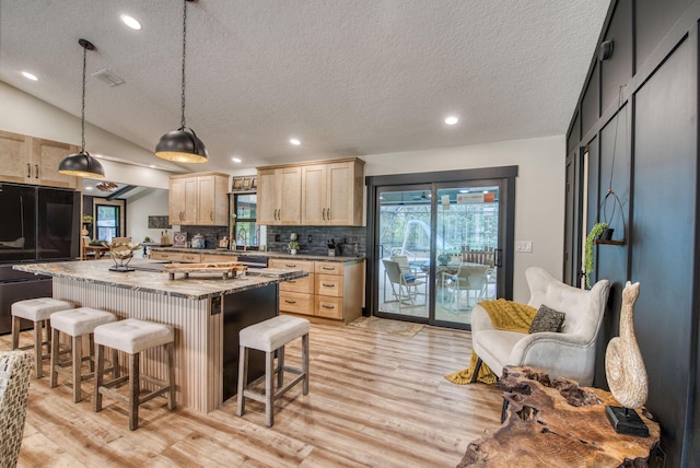 kitchen with light brown cabinets, a kitchen island, a healthy amount of sunlight, and lofted ceiling